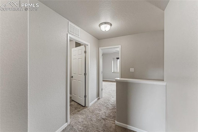 hallway with baseboards, carpet, a textured ceiling, and visible vents