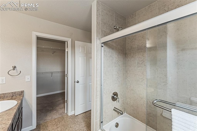 bathroom featuring vanity, baseboards, a spacious closet, and shower / bath combination with glass door