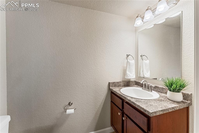 half bath with vanity, a textured wall, and toilet