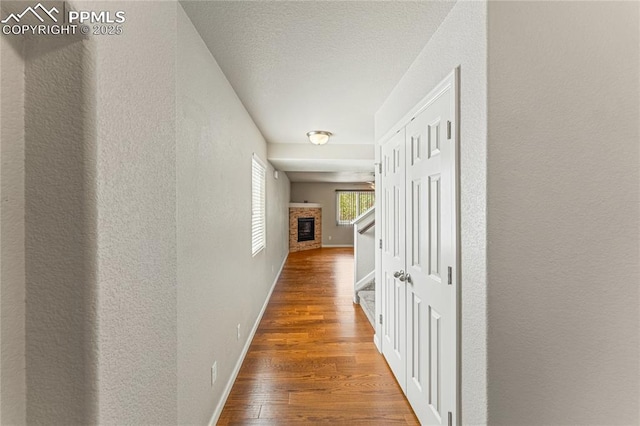 hallway with a textured ceiling, baseboards, a textured wall, and wood finished floors