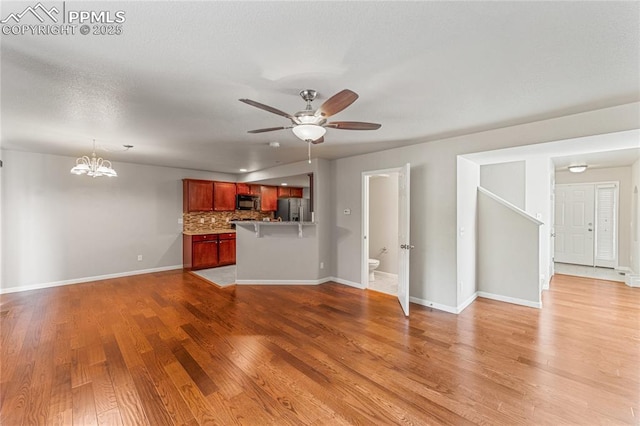 unfurnished living room with baseboards, light wood finished floors, and ceiling fan with notable chandelier