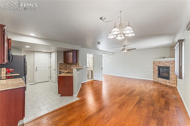 kitchen featuring a textured ceiling, baseboards, ceiling fan with notable chandelier, open floor plan, and a glass covered fireplace