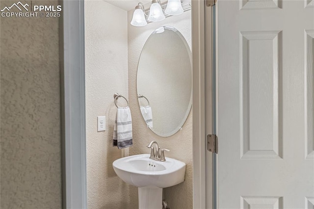 bathroom with an inviting chandelier, a textured wall, and a sink