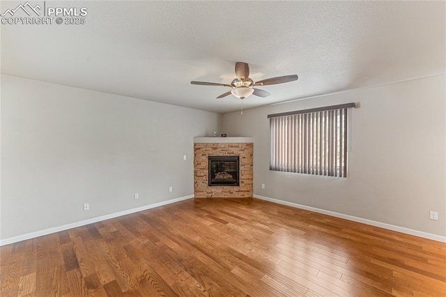 unfurnished living room featuring a glass covered fireplace, wood finished floors, baseboards, a textured ceiling, and a ceiling fan