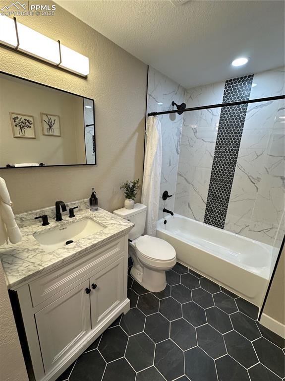 full bathroom with vanity, a textured wall, toilet, a textured ceiling, and shower / tub combo