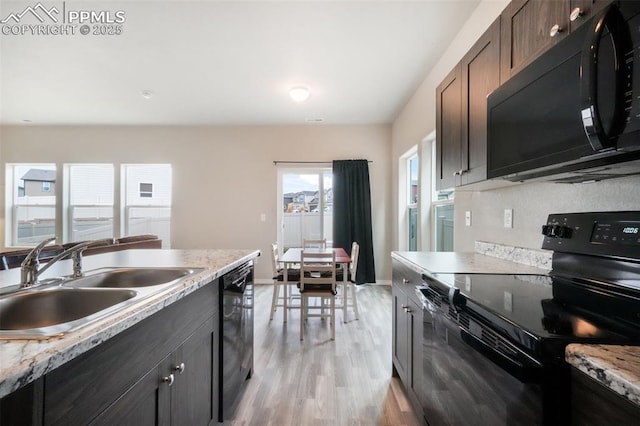 kitchen featuring light wood-style flooring, baseboards, a sink, and black appliances
