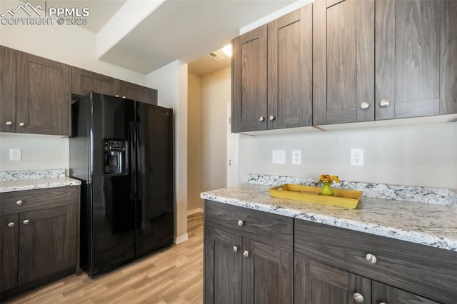 kitchen with light wood-style floors, black fridge, light stone countertops, and dark brown cabinetry