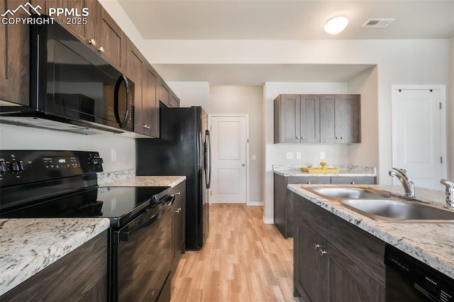 kitchen featuring dark brown cabinetry, visible vents, a sink, black appliances, and light wood-style floors