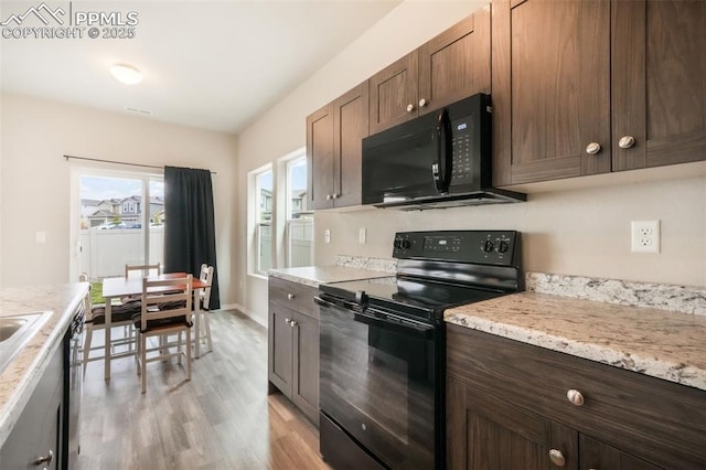 kitchen with light wood-style floors, baseboards, black appliances, and dark brown cabinets