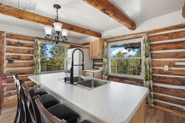 kitchen with a sink, a chandelier, beamed ceiling, light wood-style flooring, and pendant lighting