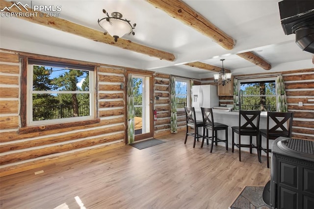 dining area with rustic walls, light wood finished floors, a chandelier, and beam ceiling