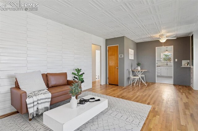 living room featuring ceiling fan, an ornate ceiling, and light wood-style flooring