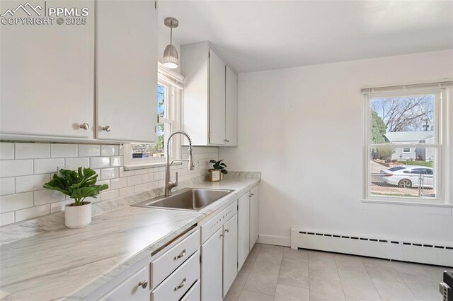 kitchen featuring white cabinets, a sink, backsplash, baseboard heating, and light countertops