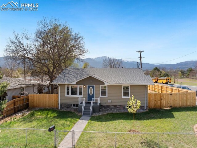 bungalow featuring a front yard, a shingled roof, a fenced backyard, and a mountain view