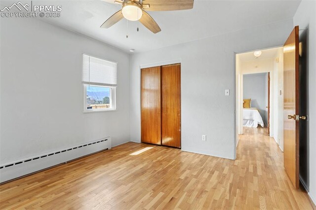 unfurnished bedroom featuring baseboard heating, ceiling fan, a closet, and light wood-type flooring