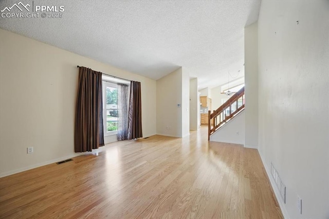 unfurnished living room featuring visible vents, baseboards, a textured ceiling, light wood finished floors, and a notable chandelier