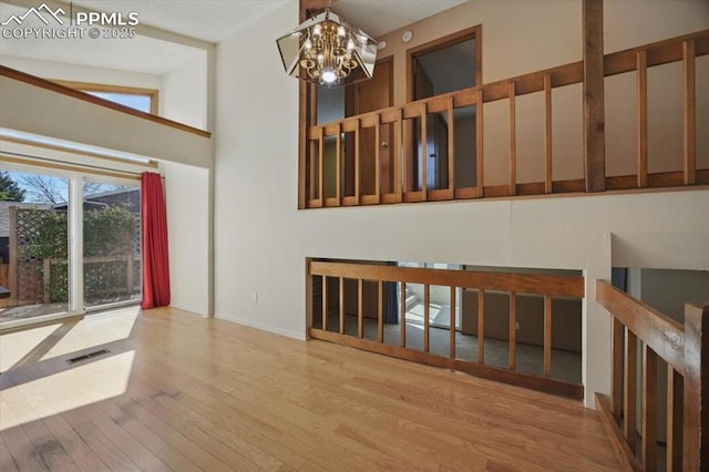interior space with an inviting chandelier, baseboards, wood finished floors, a towering ceiling, and visible vents
