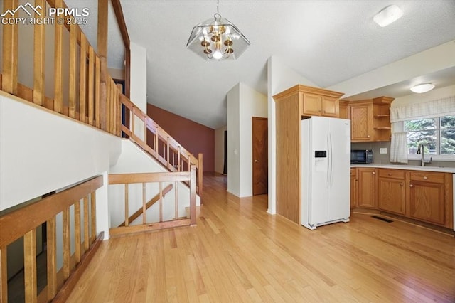 kitchen featuring black microwave, white refrigerator with ice dispenser, open shelves, a notable chandelier, and light wood-style flooring