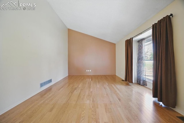spare room with baseboards, lofted ceiling, wood finished floors, and visible vents