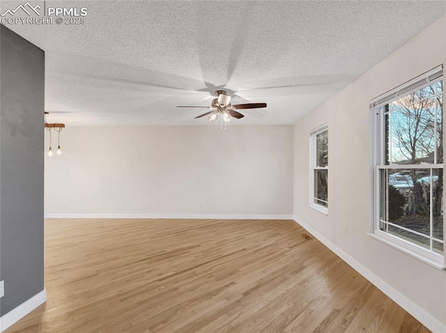 empty room with ceiling fan, baseboards, a textured ceiling, and light wood-type flooring