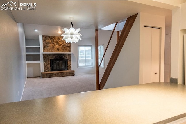 unfurnished living room featuring a stone fireplace, carpet flooring, a chandelier, and stairway
