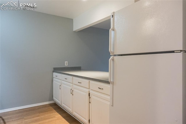 kitchen with freestanding refrigerator, white cabinets, baseboards, and wood finished floors