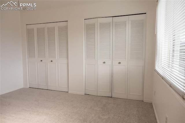 unfurnished bedroom featuring carpet flooring, baseboards, and multiple closets