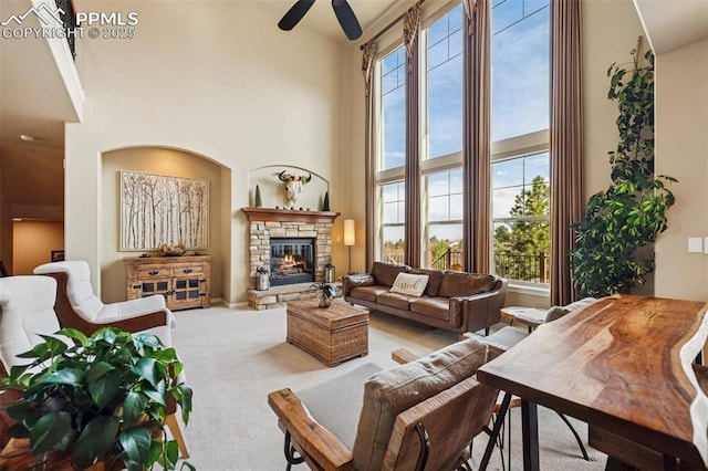 living room with ceiling fan, a high ceiling, a stone fireplace, and carpet flooring