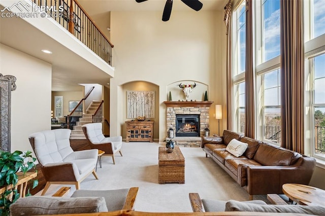 carpeted living area with stairway, ceiling fan, plenty of natural light, and a towering ceiling