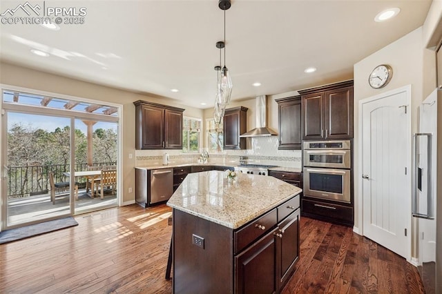 kitchen featuring stainless steel appliances, wall chimney range hood, dark brown cabinets, backsplash, and a center island