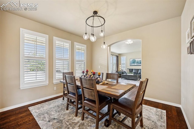dining space with wood finished floors, baseboards, and arched walkways