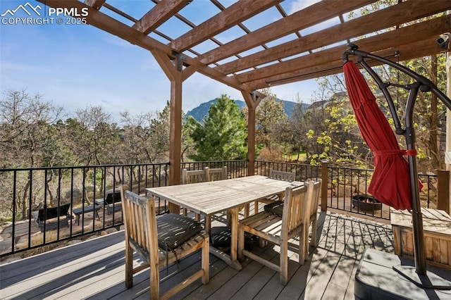 wooden deck with a mountain view, outdoor dining space, and a pergola