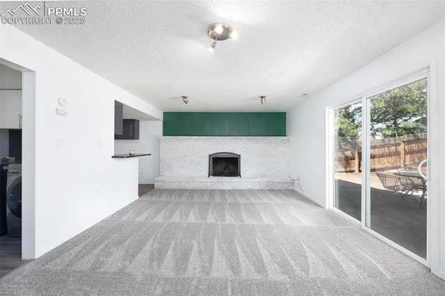 unfurnished living room featuring a textured ceiling, washer / clothes dryer, carpet flooring, and a brick fireplace