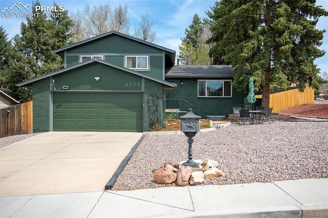 split level home with fence, concrete driveway, an attached garage, and brick siding
