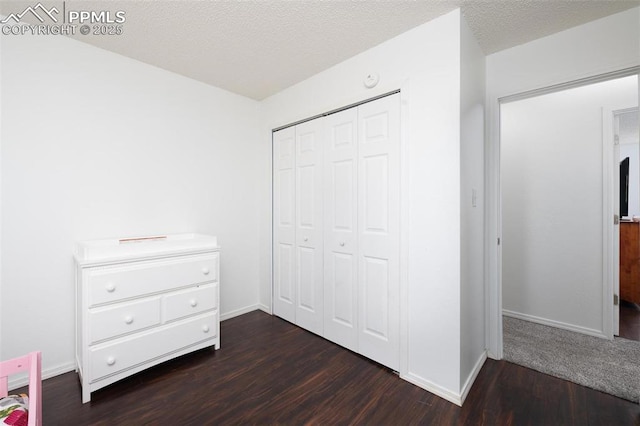 unfurnished bedroom featuring dark wood-style floors, a closet, a textured ceiling, and baseboards