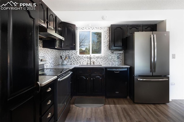 kitchen featuring decorative backsplash, under cabinet range hood, appliances with stainless steel finishes, a sink, and dark wood-type flooring