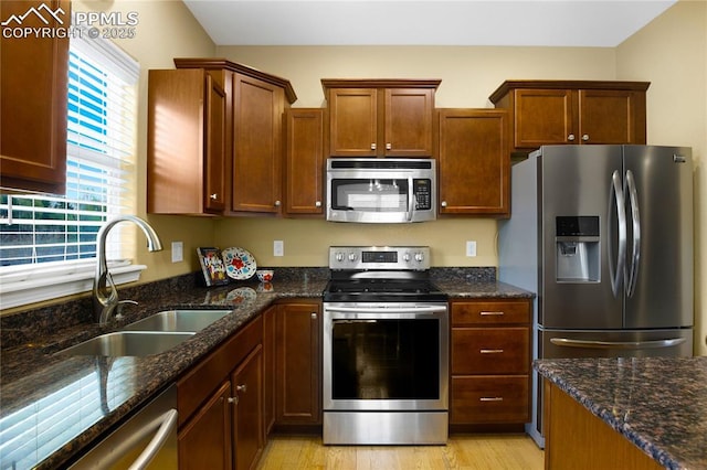 kitchen featuring light wood-style floors, appliances with stainless steel finishes, a sink, and dark stone countertops