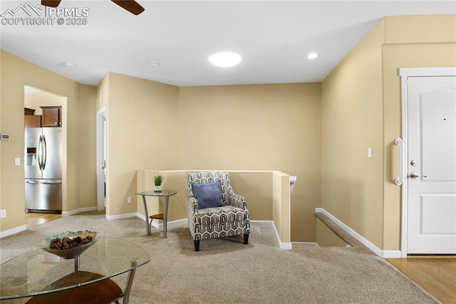 living area with baseboards, a ceiling fan, carpet, and an upstairs landing