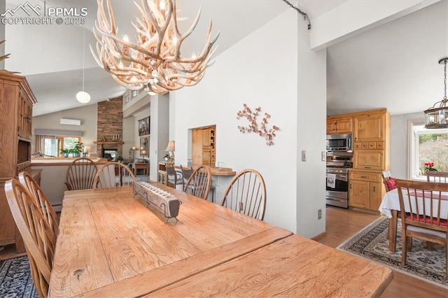 dining space with high vaulted ceiling, a notable chandelier, light wood-style floors, and a fireplace