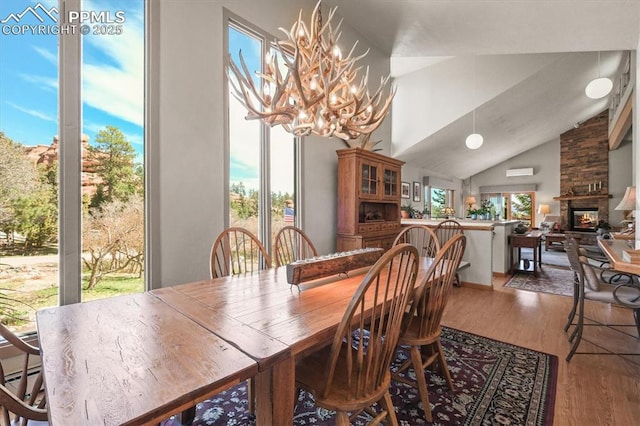 dining area with wood finished floors, a healthy amount of sunlight, a large fireplace, and an inviting chandelier