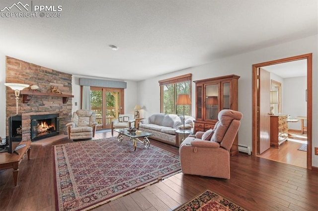living area featuring hardwood / wood-style floors, baseboard heating, and a stone fireplace