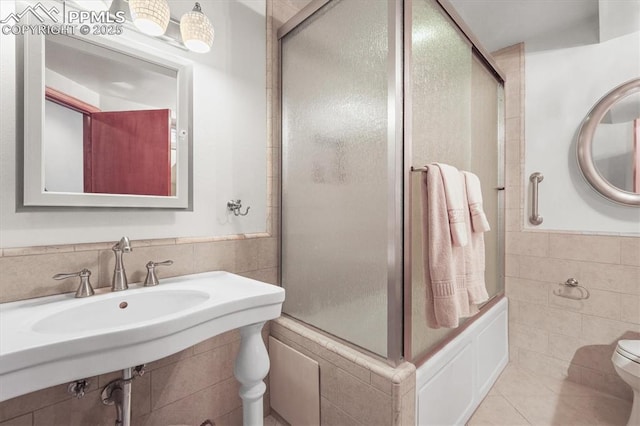 bathroom featuring tile patterned floors, wainscoting, a shower with door, tile walls, and toilet