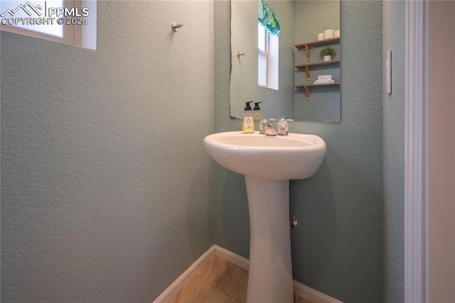 bathroom with a sink, a textured wall, and baseboards