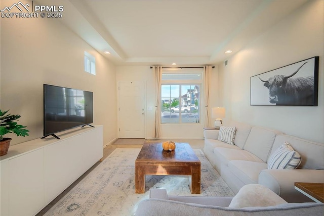 living room with baseboards, recessed lighting, light wood-style flooring, and a tray ceiling