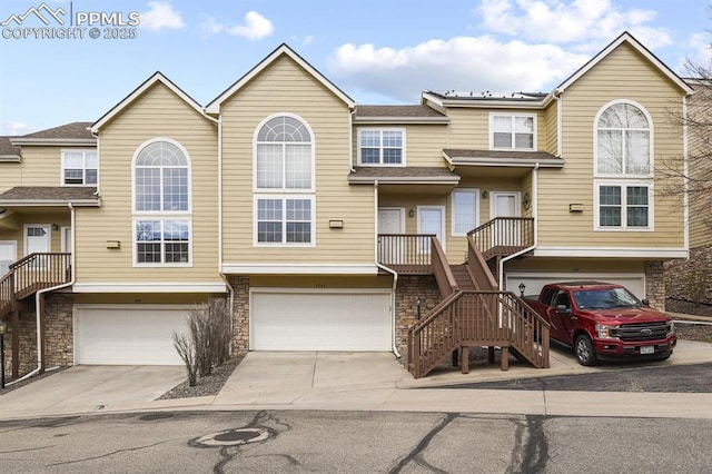 view of property featuring an attached garage, stone siding, stairs, and driveway