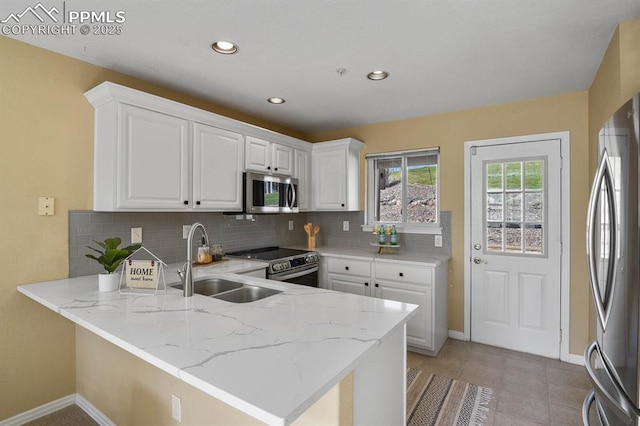 kitchen featuring stainless steel appliances, a peninsula, a sink, baseboards, and backsplash