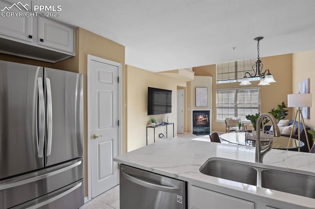 kitchen with a sink, open floor plan, a glass covered fireplace, an inviting chandelier, and appliances with stainless steel finishes