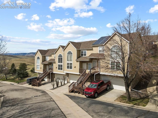 view of property featuring an attached garage, stairway, roof mounted solar panels, and driveway