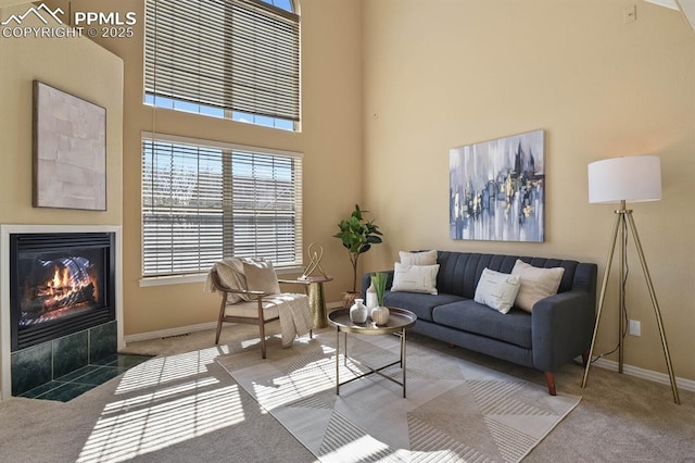 carpeted living area with baseboards, a tile fireplace, and a high ceiling