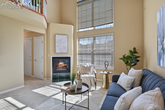 living area with a towering ceiling, a tiled fireplace, baseboards, and carpet floors